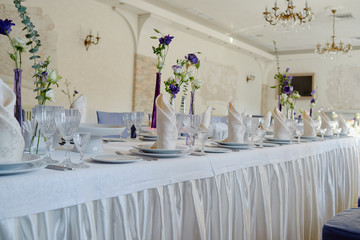 Table setting with white plates, napkins, wineglasses, cutlery and flowers on table, copy space. Place setting at wedding reception. Table served for wedding banquet in restaurant