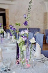Beautiful floral arrangement on wedding table in restaurant, copy space. Bouquet of pink roses, purple eustoma and greenery in glass vases. Luxury wedding decorations