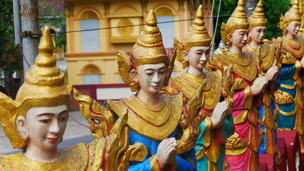 Fototapeta na wymiar group of six monk statues at the entrance of a big temple wearing traditional golden hats with hands folded for praying, Mawlayine, Myanmar, Asia