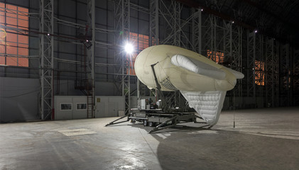 Small airship on a mooring platform in a giant aircraft hangar