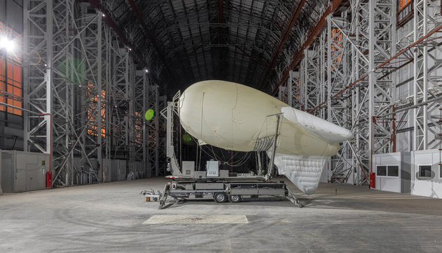 Small blimp on a mooring platform inside a giant airship hangar. Side view