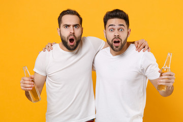 Shocked young men guys friends in white empty blank t-shirts posing isolated on yellow orange wall...
