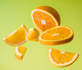 Bright green background, slices of orange are different sizes in air. Vitamin C. Healthy nutrition. Citrus.