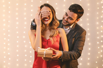 Elegant man covering his girlfriend's eyes and giving her gift box