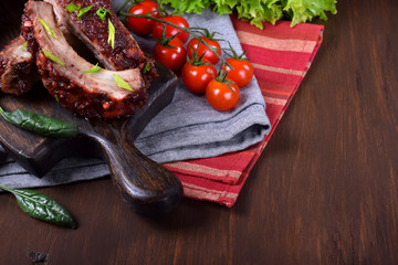 Roasted pork ribs with glazing served on the wooden board surrounded by the vegetables and herbs