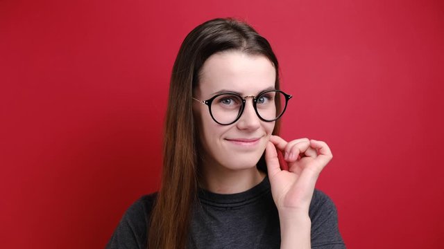 Young woman zips her mouth shut, promises to keep secret,  holds fingers near cheek, makes promise, hides information dressed in grey t-shirt, isolated over red background. Keeping quiet concept