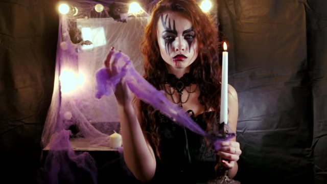 Girl with Halloween makeup approaches the camera holding a burning candle in her hand.