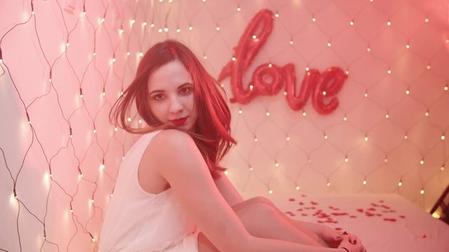 Girl sexy stare towards the camera with a Love sign in background 4K. Middle shot of a female person in focus with decoration lights in background.