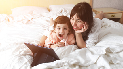 Mother with daughter are happy to be together. Watching cartoons on the digital tablet pc.