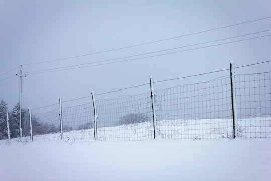 Zaun aus Maschendraht mit Stromleitung und Schnee