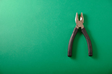 Pliers with black handles on a green background, top view