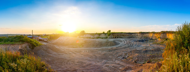 The excavator stands in a clay quarry for a small brick factory. Evening sunshine in industrial landscape. Panoramic view.