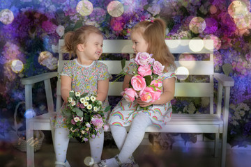 little twin girls in the garden on a bench against the background of a floral wall with bouquets of flowers in their hands