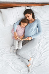 Loving pregnant mom reading book to her little kid