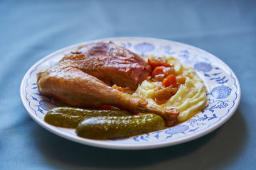 Roasted chicken leg from small organic farm served on the rustic plate with mashed potatoes with butter and pickled cucumber. Traditional homemade family sunday lunch typical for czech cuisine.