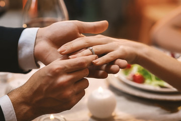 Fototapeta na wymiar Man Putting Engagement Ring On Girfriend's Finger After Proposal In Restaurant