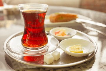Turkish tea in traditional glass on tray with baklava, sugar, lemon and succades. Outdoor shot