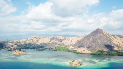 Fototapeta na wymiar A drone shot of a paradise island with some boats anchored around in Komodo National Park, Flores, Indonesia. Green middle part of the island turns into white sand beach and further into turquoise sea