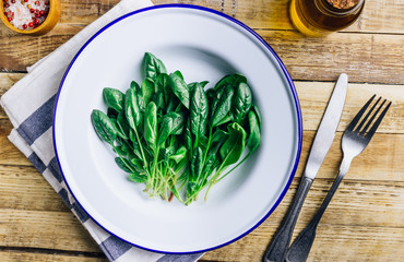 Fresh green baby spinach on plate on wooden rustic table. Healthy diet, vegetarian food concept.
