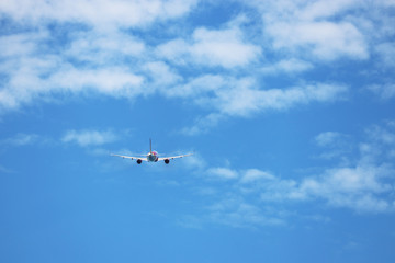 Airplane flying in the blue sky on background of white clouds, rear view. Twin-engine commercial plane during the turn, turbulence and travel concept