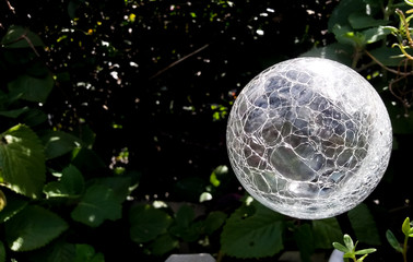Solar garden light with sphere shape and an abstract pattern design reflecting the sun during the day as it powers with dark blurred foliage in the background