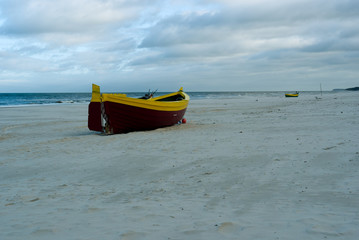 A maroon yellow maritime cutter stands on the beach in the sand