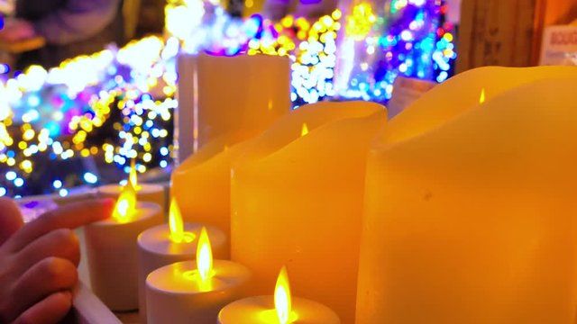 Mano de ni&ntilde;o tocando la llama de una velas navide&ntilde;as con llama falsa con fondo de luces de colores
