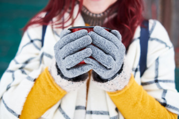 Girl holding winter cup close up on green background. Woman hands in grey gloves holding a cozy mug with hot tea or coffee. Winter time concept