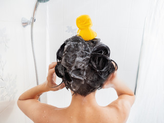Naked woman with short hair takes a shower. Woman washes her hair with shampoo. Yellow rubber duck...
