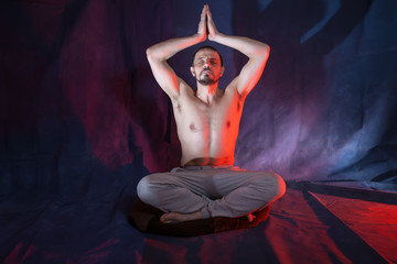 A man sits in a lotus position. Male European 40-45 years old. A man is engaged in meditation. The man raised his arms above his head. Magic and occultism.