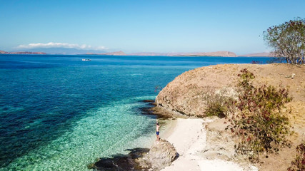 Fototapeta premium A drone shot of a man standing on a big boulder on a paradise island in Komodo National Park, Flores, Indonesia. Man spreads his arms in a gesture of freedom and happiness. Idyllic island hopping.