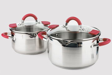 Stainless casserole with glass lid and red handles on grey background.