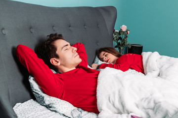 Cute couple in red pajamas lying in bed together, sleeping, relaxing.
