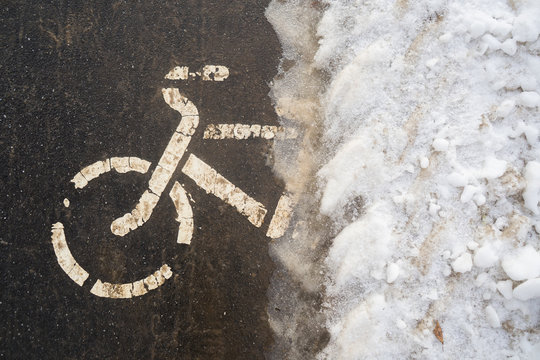 Bicycle path in winter under the snow. The bike season is closed due to ice. Biking in cold weather, cycling in cold weather. Bicycle stencil on the pavement