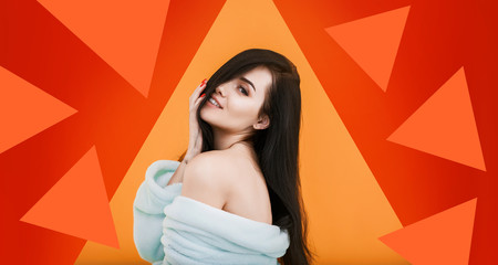 Young sexy girl in bathrobe with bare shoulders posing on bright geometric orange background. Pretty woman expresses joyful emotions. Free space for text. Trends 2020.