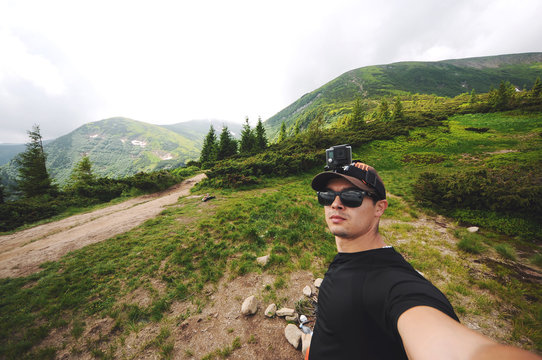 Handsome hiker taking a selfie hiking a mountain using his smartphone.Tourist with action camera on his head