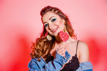 Beautiful brunette girl with blue makeup, pigtails and a sleeveless denim vest posing on a red...