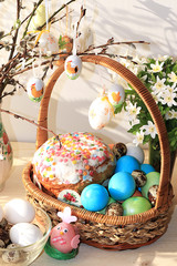 Easter composition on a sunny rustic table. Happy blue eggs in a basket, Easter cake and sweets, spring flowers. Spring festive background.
