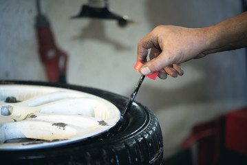 Worker of auto service station is glueing by sealant a wheel rim close up. Defocused image.