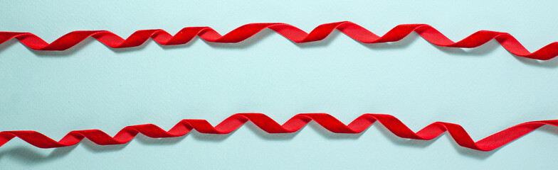 White gift box with a red velvet ribbon bow along the frame on blue flat lay