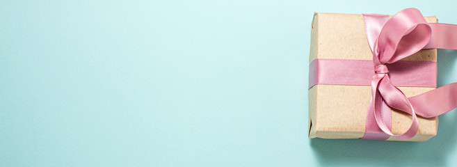 Banner of brown paper gift box with a purple satin ribbon bow on blue flat lay