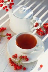 Tea with viburnum in a white cup, teapot ,viburnum brush on a white table.