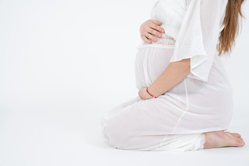 Fototapeta na wymiar Waiting for a baby. Close-up of pregnant woman in white underwear touching her belly while sitting in on the ground