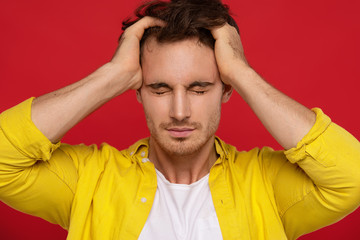 man with headache in yellow shirt holding head with closed eyes isolated on red background