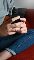 Junge Frau schreibt eine Nachricht auf dem mobile Handy sitzend auf dem Sofa zuhause