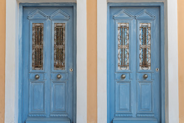 Two similar old wooden doors on orange wall. The traditional colorful design in island Symi in Greece. 