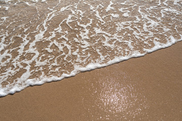The foam of wave on the sand. Closeup image of waves roll over of perfect golden sandy shore.	