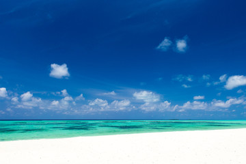 Fototapeta premium Beach with white sand, turquoise ocean water and blue sky with clouds in sunny day. Natural background for summer vacation. Panoramic view.