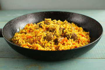 Dish of oriental cuisine - pilaf with lamb in a pan, on a wooden background.