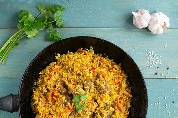 Dish of oriental cuisine - pilaf with lamb in a pan, on a wooden background.